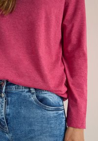 Långärmad rosa skjorta gjord av mjukt tyg, parat med ljusblå slitna jeans i denim med framficka och knappstängning.