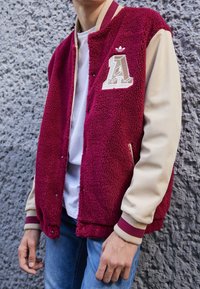 Vinröd collegejacka i fleece med beige ärmar, ribbade muddar och ett broderat bokstaven 'A' samt en logotyp, utrustad med tryckknappar och sidofickor.