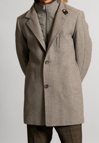 Beige visgraatjas met een reverskraag, twee knopen en een kraag. Binnenste telefoonjack, grijs met vulling. Geweven stof.