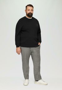 Schwarzer Pullover mit Rundhalsausschnitt und kleinem Logo, kombiniert mit grauen Karo-Hosen und weißen Sneakern, was ein lässiges Outfit ergibt.