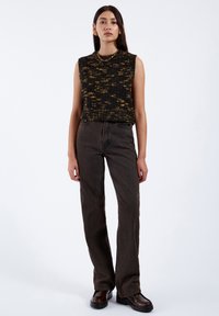 Svart och gul prickig ärmlös stickad topp, i kombination med bruna raka jeans och mörkbruna kraftiga stövlar, med en klassisk passform.