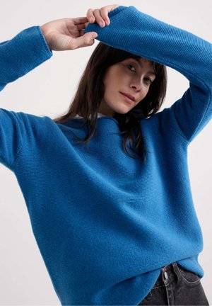 Blue knit sweater with a loose fit, ribbed cuffs, and a smooth texture. A slight droop at the waist adds to its relaxed appearance.