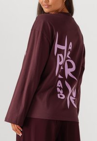 Bordeaux langslavige shirt met grote paarse grafische tekst op de rug, ronde halslijn en een ontspannen pasvorm. Gemaakt van zachte stof.