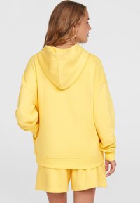 Felpa gialla con cappuccio realizzata in tessuto morbido, caratterizzata da una vestibilità comoda e spalle scese, abbinata a shorts coordinati.