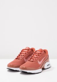 Red mesh athletic shoes with a smooth shoe cap, white midsole, and black rubber outsole; features a prominent logo on the side.