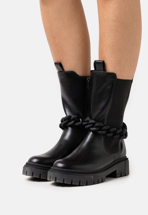 Stivaletti neri in pelle liscia con suola spessa e dettaglio in catena lungo la parte superiore. Presentano una zip laterale e linguette di trazione.