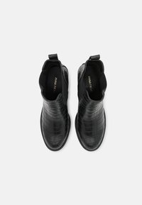 Un par de botas negras de piel de cocodrilo con textura, con paneles laterales elásticos y lengüetas de agarre, vistas desde arriba sobre un fondo blanco.