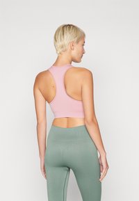 Soutien-gorge de sport rose clair avec un design dos nageur, fabriqué en tissu extensible. Associé à un legging taille haute vert, montrant une texture lisse.