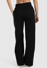 Schwarze weit geschnittene Hose mit einem elastischen Bund, glatter Textur und einem entspannten Schnitt, der bis zu den Knöcheln reicht. Keine sichtbaren Taschen.