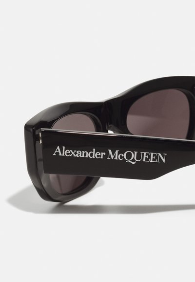 Occhiali da sole neri oversize con finitura lucida, dotati di lenti scure e marchio "Alexander McQueen" in argento sulla tempia.