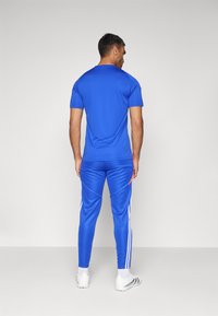 Blauwe sport t-shirt met korte mouwen en bijpassende blauwe broek met witte strepen langs de benen. Het materiaal lijkt glad en lichtgewicht.