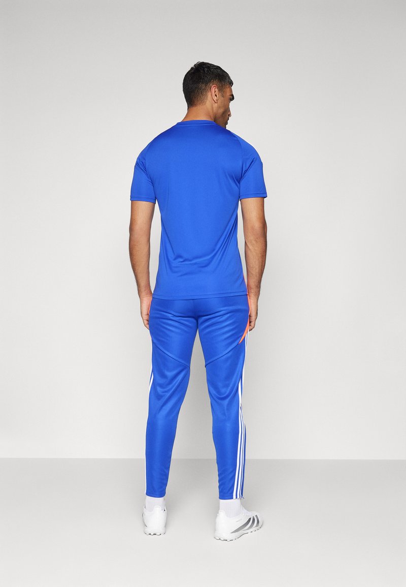 Blaues Sport-T-Shirt mit kurzen Ärmeln und passende blaue Hose mit weißen Streifen entlang der Beine. Das Material wirkt glatt und leicht.