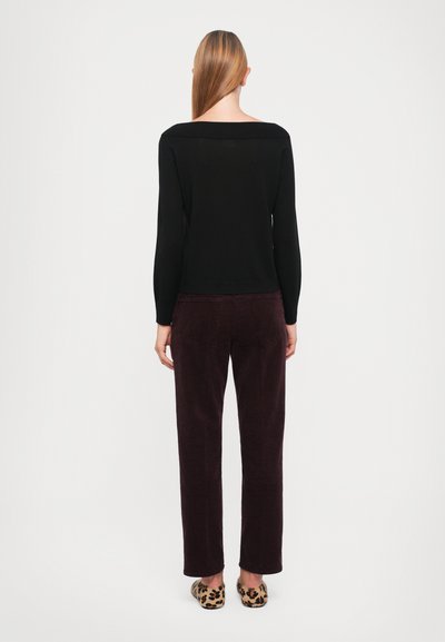 Schwarzes Strickoberteil mit weitem Ausschnitt, kombiniert mit tiefpflaumefarbenen Cordhose. Braune Loafers im Leopardenprint runden das Outfit ab.