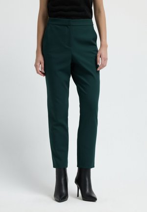 Donkergroene op maat gemaakte broeken met een slim fit, gemaakt van een gladde stof. Heeft een hoge taille en zijzakken, gecombineerd met zwarte haklaarzen.