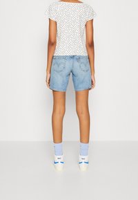Top blanco con estampado floral y mangas cortas, combinado con pantalones cortos de mezclilla de color azul claro. Completan el look unas zapatillas blancas con detalles azules.