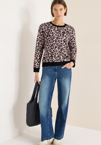 Różowo-czarny sweter w panterkę z długimi rękawami i czarnym prążkowanym obszyciem. Jasnoniebieskie jeansy o szerokich nogawkach oraz czarna torba typu tote.