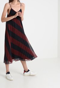 Svart och vinröd randig midiklänning med tunna axelband och veckad design, parat med vita sneakers med röda och navy detaljer.