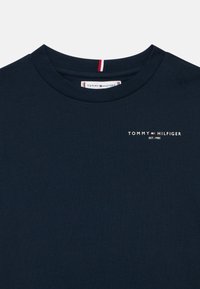 Tamsiai mėlynas apvalaus kaklo marškinėliai su mažuoju Tommy Hilfiger logotipu ir tekstu "EST. 1985" viršutiniame kairiajame krūtinės kampe.