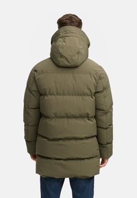 Parka acolchada de color verde oliva con capucha, que presenta costuras horizontales y un corte recto. La tela tiene una textura suave y es resistente al agua.
