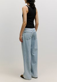 Zwarte geribbelde tanktop, blauwe wijdvallende denim jeans, weergegeven vanaf de achterkant, met twee achterzakken en een relaxte pasvorm.