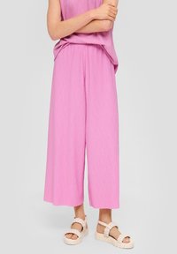 Růžové široké kalhoty s krabatou strukturou, zkombinované s béžovými pletenými sandály. Oblečení má volný střih a elastický pas.