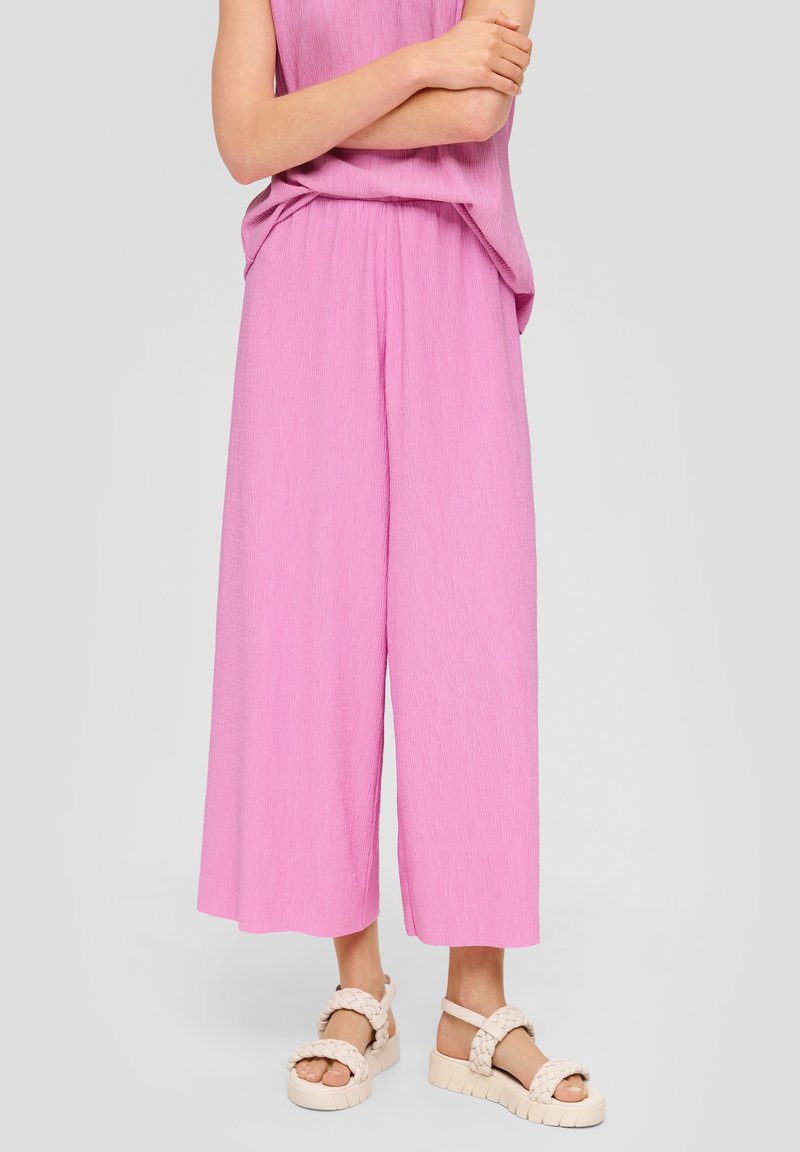 Růžové široké kalhoty s krabatou strukturou, zkombinované s béžovými pletenými sandály. Oblečení má volný střih a elastický pas.