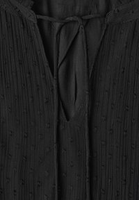 Haut en tissu noir texturé avec côtes verticales et petits points en relief, avec une fermeture à cordon au niveau de l'encolure fendue.
