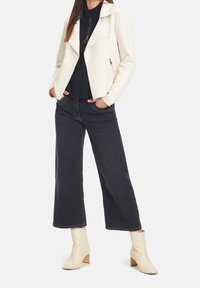 White faux leather motorcycle jacket with a wide collar, paired with a black knit top, black wide-leg jeans, and beige block-heeled ankle boots.