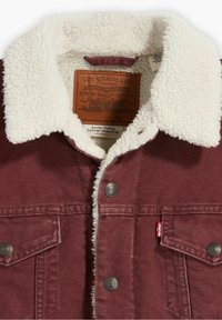 Mörkröd Levi's jacka med vit sherpa-fleecekrage, metallknappar, bröstfickor och synlig Levi's läderlogotyp inuti kragen.