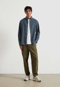 Koszula zapinana na guziki w ciemnoniebieskim kolorze, biała koszulka pod spodem, oliwkowe spodnie i szare sneakersy z akcentami. Prosty design, luźny krój.