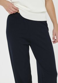 A tengerészkék kötött sportnadrág rugalmas derékkal és laza szabással rendelkezik, puha anyagból készült, sima textúrával és minimalista részletekkel.