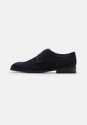 Navy suede dress shoe with a smooth finish, lace-up closure, rounded toe, and a low, dark wooden heel. Simple, clean design.