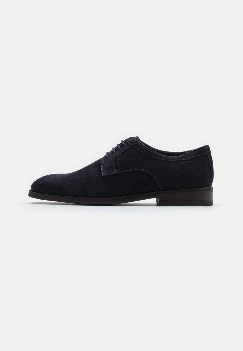 Scarpa da dress in suede blu navy con finitura liscia, chiusura con lacci, punta tonda e tacco basso in legno scuro. Design semplice e pulito.