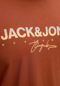 Rauha värvi puuvillane T-särk, millel on erksad valged kirjavead "JACK&JON" ja iseloomulik disainielement, sujuva tekstuuri ja ümar kaelus.