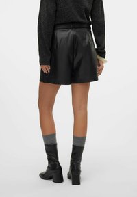 Sorte lædershorts med en glat tekstur, der har høj talje og flad front. Parret med knælange sorte læderstøvler og grå ribbede sokker.