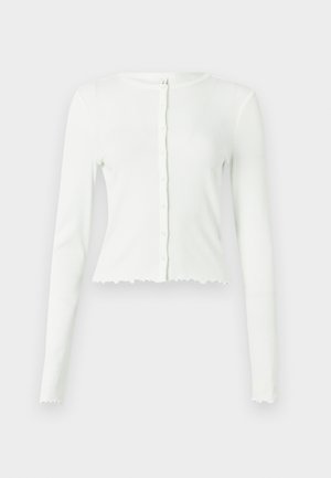 Weißes langärmeliges, geripptes Cropped-Top mit rundem Ausschnitt und Knopfverschluss. Mit gewelltem Saum und tailliertem Schnitt.