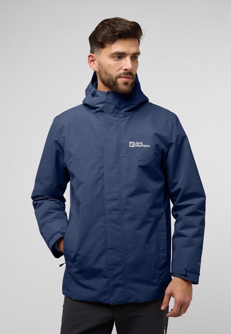 Giacca impermeabile blu navy con colletto alto, cappuccio regolabile e dettaglio del logo sul petto. Il tessuto appare liscio con una finitura opaca.