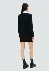 Schwarzer, flauschiger Pullover kombiniert mit einem schwarzen Minirock. Das Modell trägt klobige, schwarze Kampfstiefel; das Outfit zeigt einen lässigen, geschichteten Look.