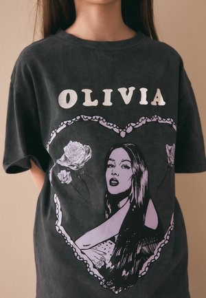 Persoană care poartă un tricou negru cu inscripția „OLIVIA” în alb și o grafică în formă de inimă cu o femeie cu păr lung și trandafiri în interiorul inimii.