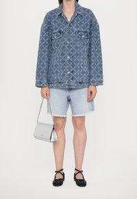 Kurtka dżinsowa w jasnoniebieskim kolorze z wzorem diamentowym, zestawiona z jasnymi dżinsowymi szortami o postrzępionym dole. Trzyma srebrną torebkę; nosi czarne baleriny.