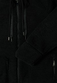 Veste en polaire noire avec fermeture éclair à l'avant, poche zippée, manches à poignet et cordons noirs portant l'inscription "CRÉEZ VOTRE PROPRE CHEMIN."