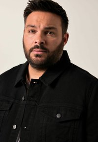 Svart denimjacka med metallknappdetaljer, två bröstfickor och spetsig krage. Tyget har en texturerad yta.