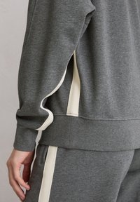 Szara bluza z miękkiego materiału, z kremowymi akcentami po bokach, prążkowanymi mankietami i luźnym krojem z teksturowanym wykończeniem.