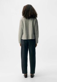 Maglione grigio in lana con vestibilità rilassata, maniche a coste e dettaglio della cucitura sul retro, abbinato a jeans scuri e scarpe slip-on nere.