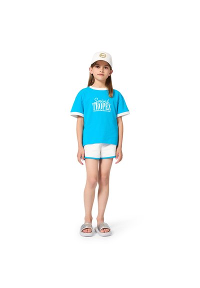 Turquoise katoenen T-shirt met witte manchetten, met "Saint Tropez"-afbeelding. Gecombineerd met witte korte broek en zilveren slides.