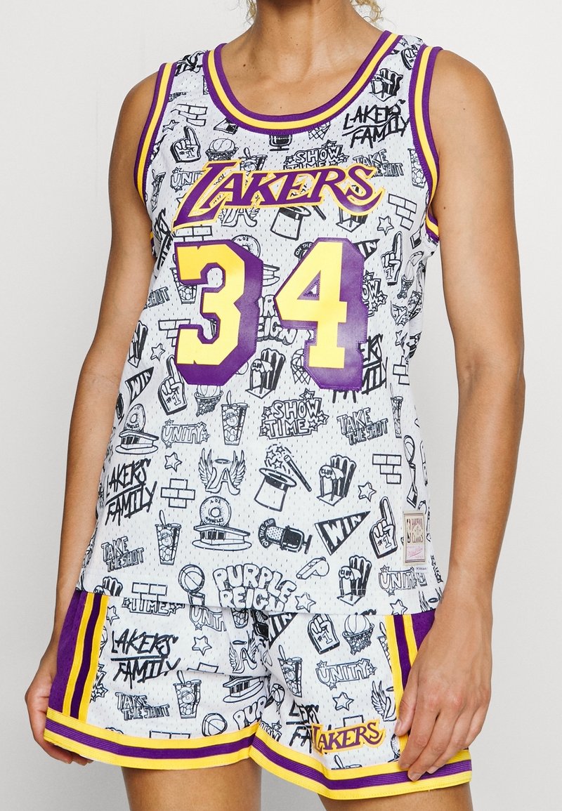 Femme portant un maillot et un short de basketball blanc des Lakers avec le numéro 34 et des griffonnages noirs à thème sportif partout.
