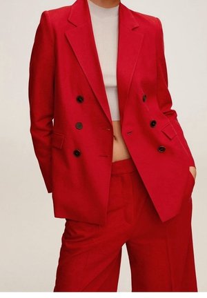Personne portant un blazer rouge à double boutonnage et un pantalon assorti avec un top court côtelé blanc, main dans la poche.