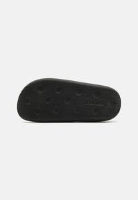 Sort gummisål med en tekstureret overflade og cirkulære grip mønstre, med et forhøjet logo "Levi's" nær hælområdet.