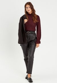 Bordeaux neulottu villapusero, jossa on röyhelöhihat, yhdistetty korkeavyötäröisiin mustiin keinonahkapö trousers. Malli pitää mustaa bleiseriä.