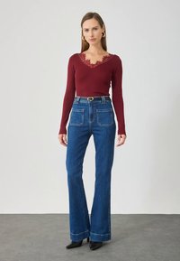 Burgunderfarget ribbestrikket langermet topp med blondedetaljer ved utringningen, kombinert med høytlivs blå vidde jeans med store baklommer og belte.